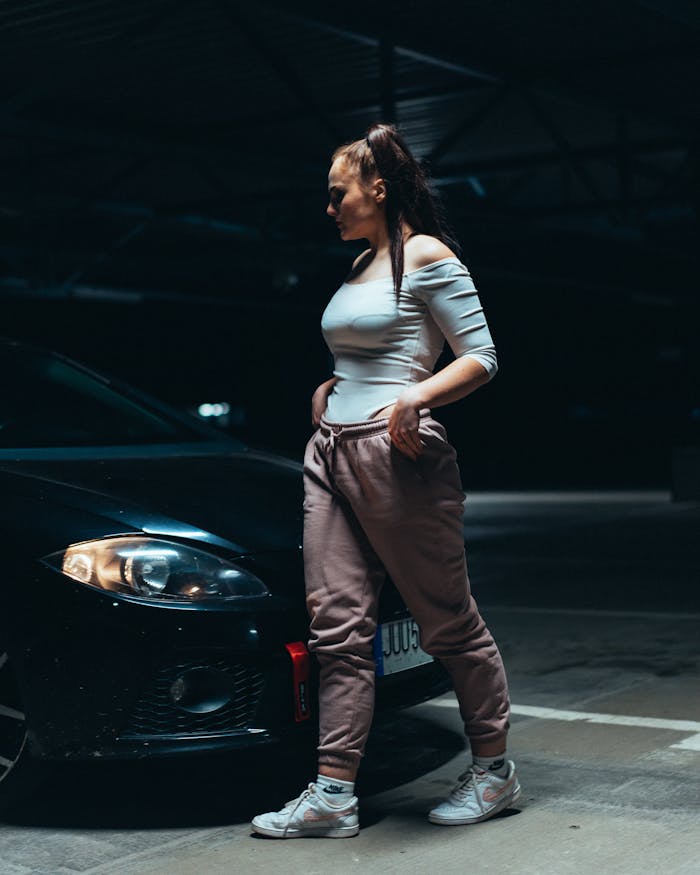 journey-02 A fashionable woman poses confidently beside a car in an urban parking lot at night.