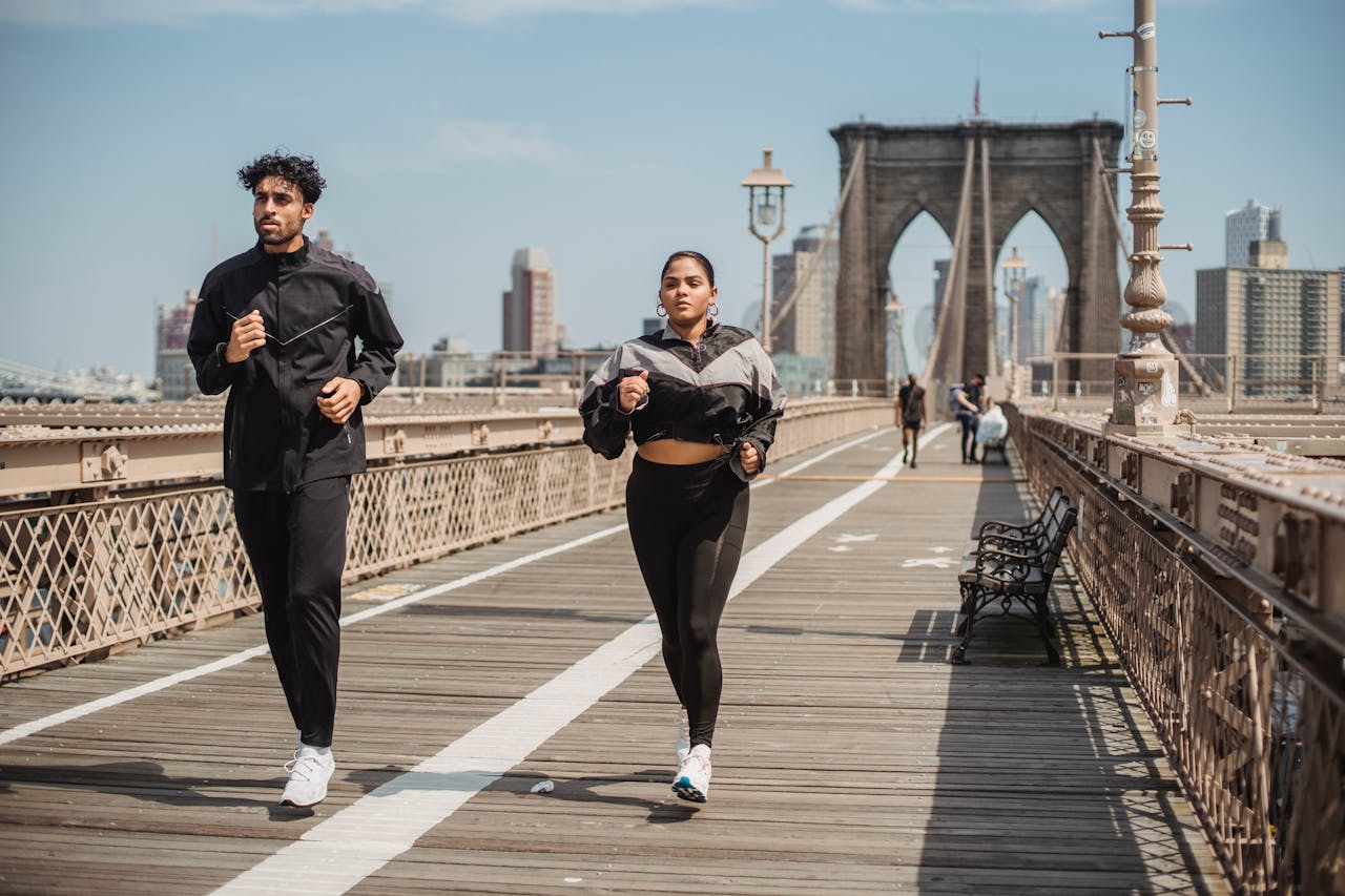 vision Two adults jogging on Brooklyn Bridge with city skyline in the background, showcasing health and vitality.